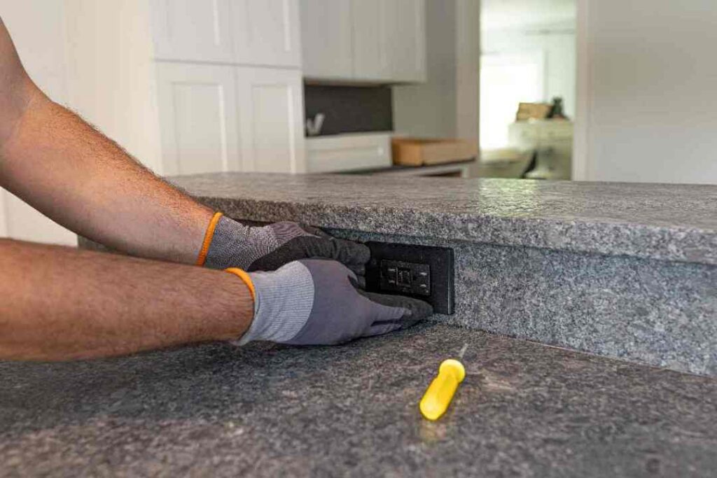 Electrician installing a GFCI outlet in a granite kitchen countertop during a remodel