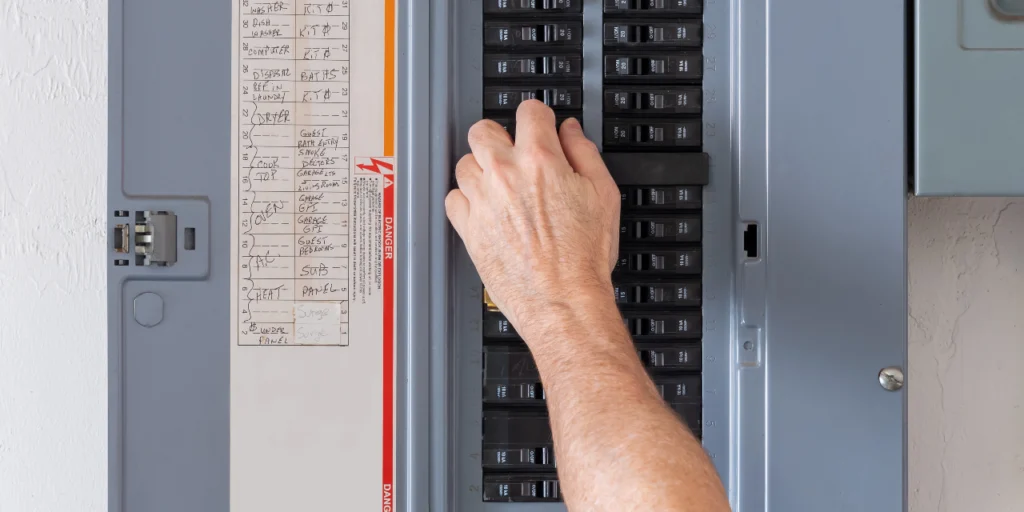 A hand resets a breaker inside an open electrical panel with a labeled circuit directory, the first check during home electrical troubleshooting.