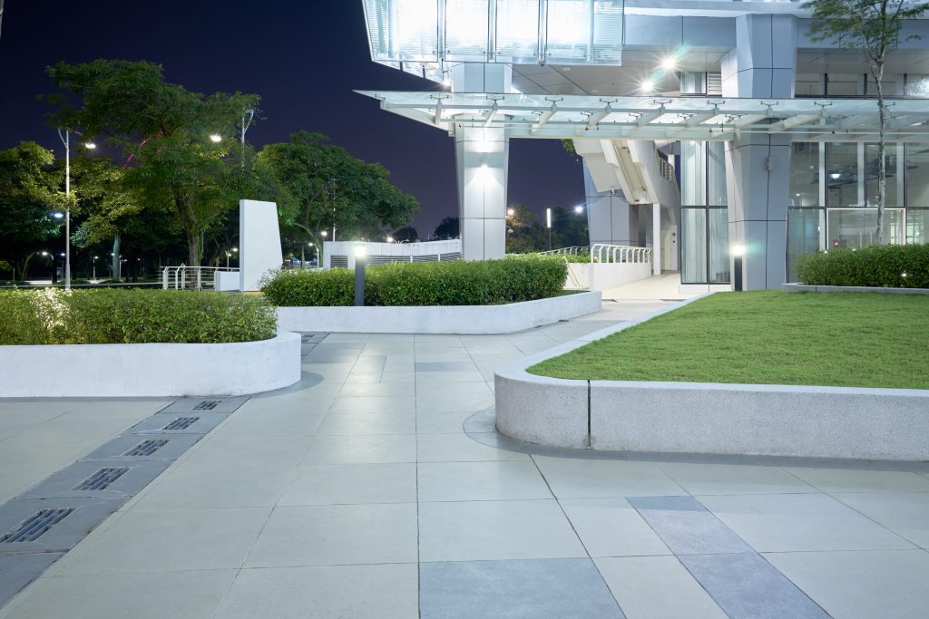 A glass-fronted commercial building at night with its entry walkway and landscaping lit, the result of a commercial lighting installation.