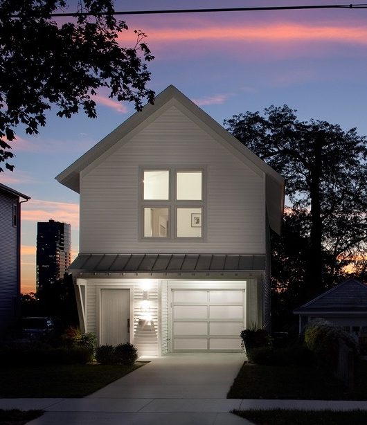 A two-story house, in West Michigan, with lit windows against a pink dusk sky, the kind of home a battery backup system keeps running when the grid goes down.
