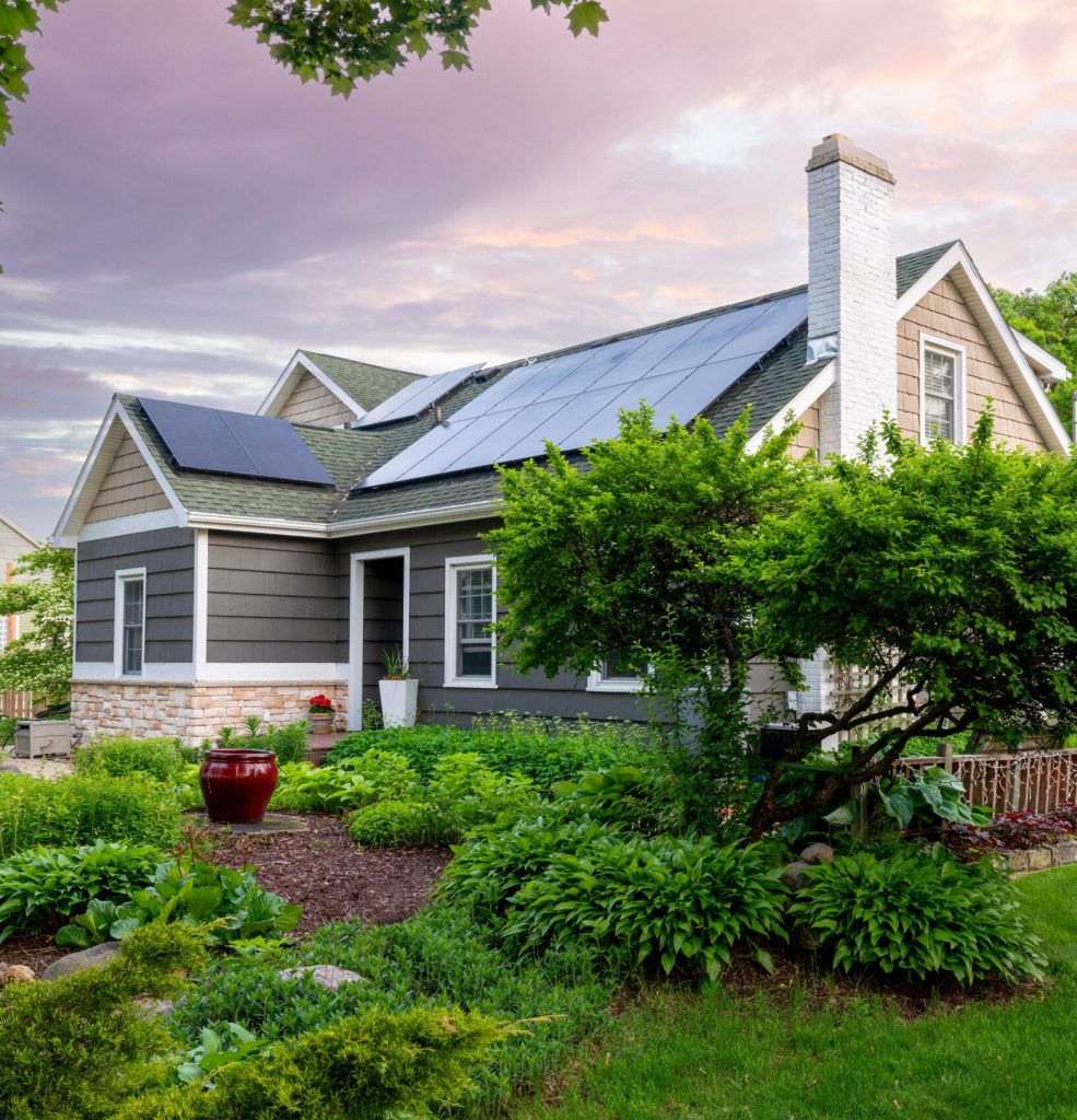 A home with rooftop solar panels rising above a full garden of shrubs at dusk, showing how an array sits on the roof while preserving the yard's beauty.