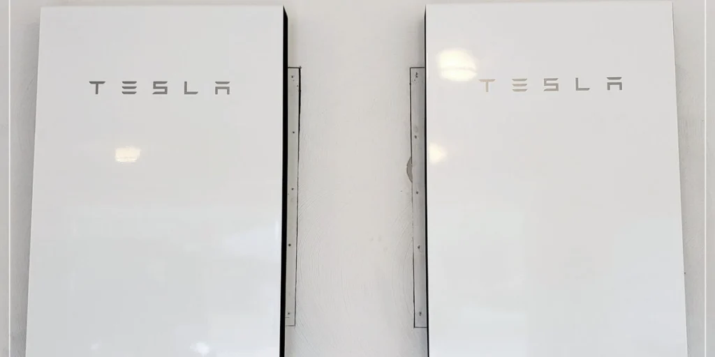 Two Tesla Powerwall units mounted side by side on an interior wall, paired capacity sized to carry a West Michigan home's essentials through an outage.